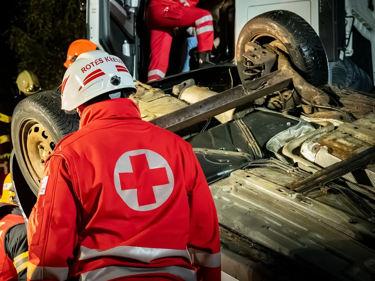 Einsatzkraft des Roten Kreuzes von hinten an einem umgestürzten Fahrzeug bei einer Nachtübung