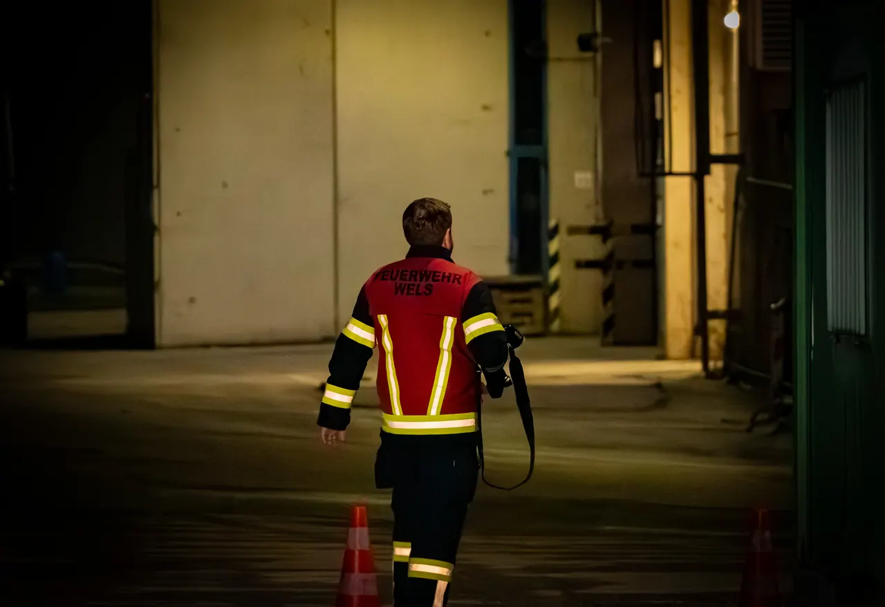 Einsatzkraft der Feuerwehr von hinten, auf dem Weg durch eine nächtliche Halle