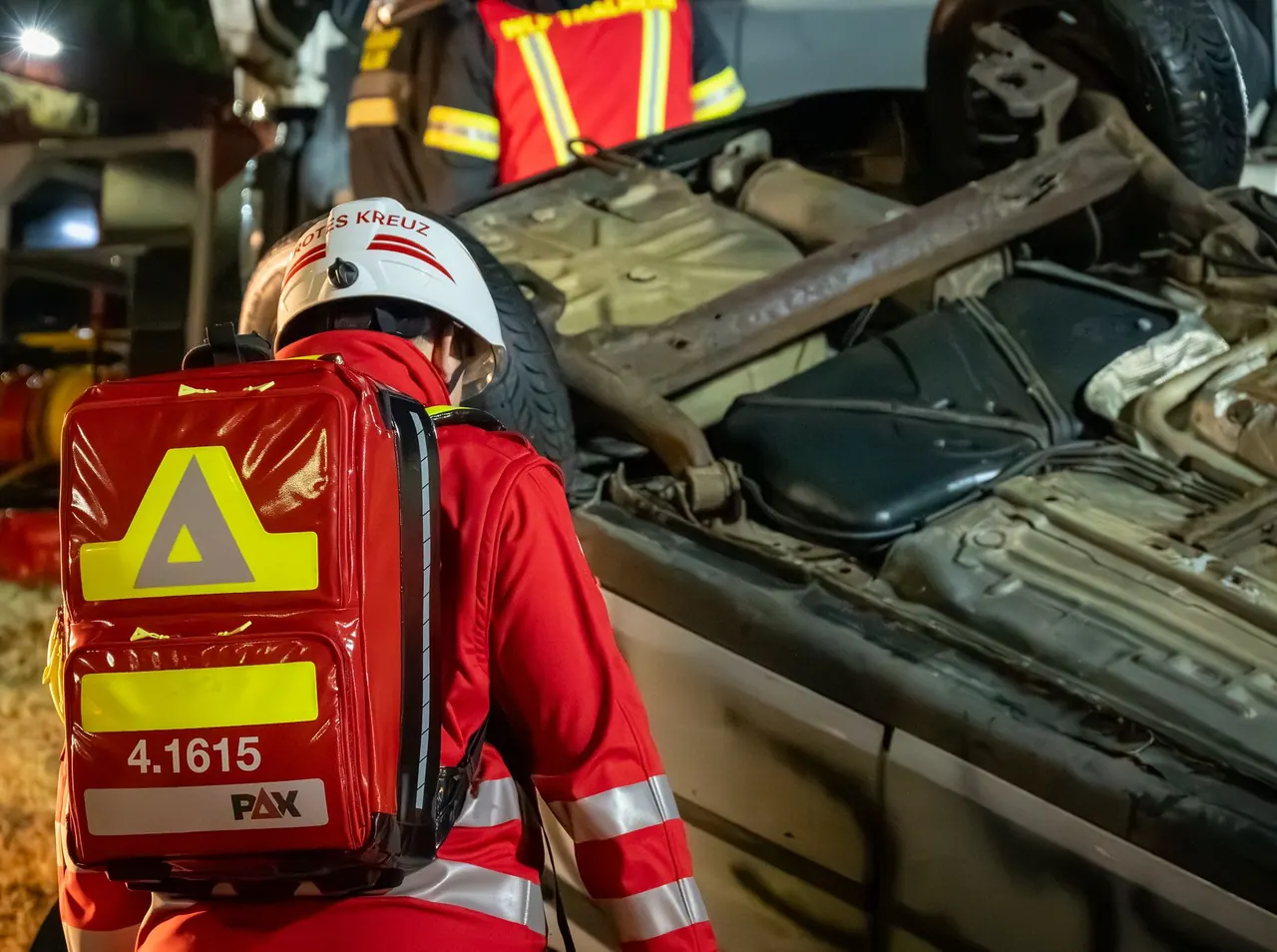 Notfallrucksack auf dem Rücken einer Einsatzkraft neben einem umgestürzten Fahrzeug